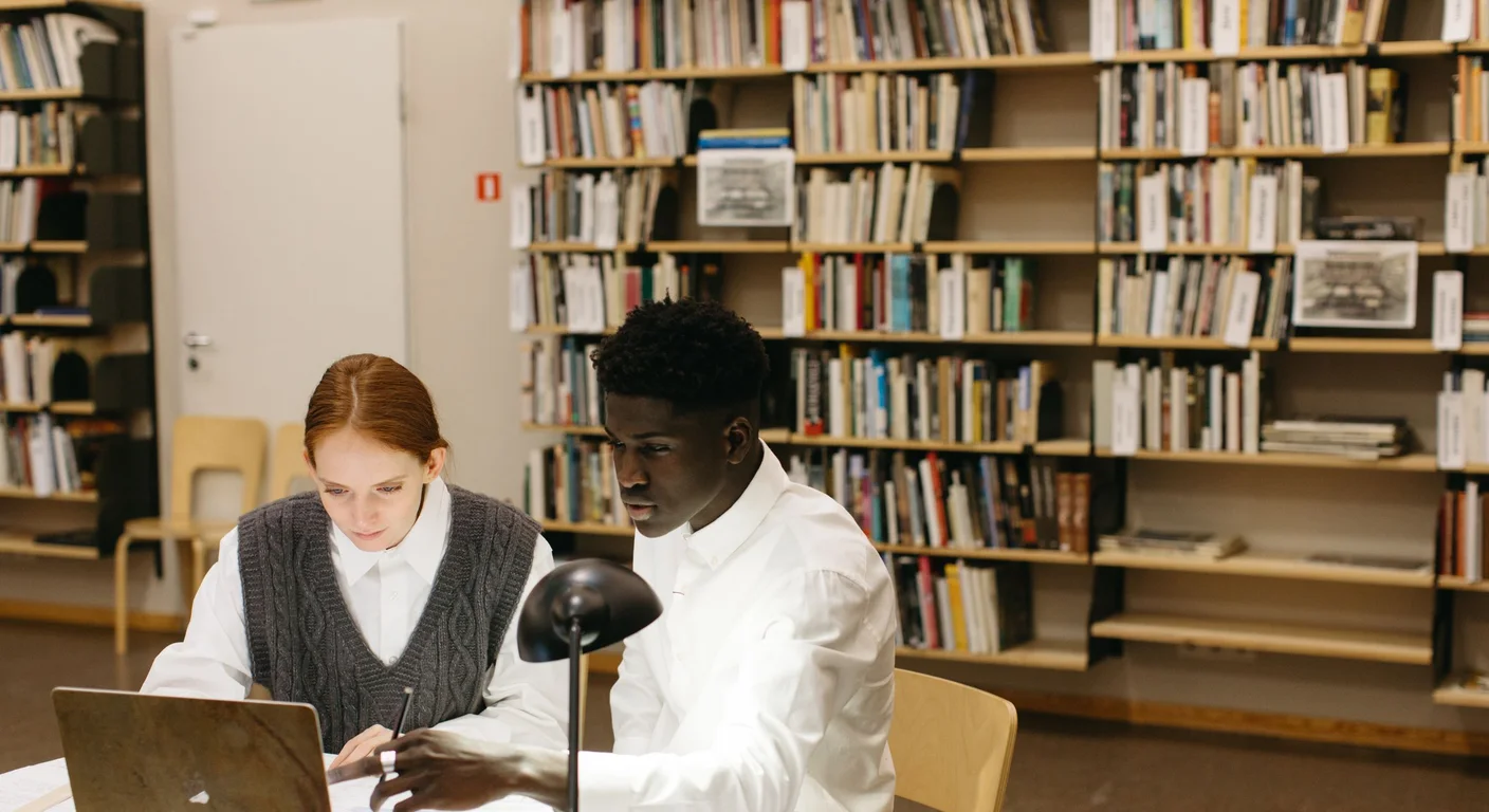 Two students comparing research on a laptop in a library